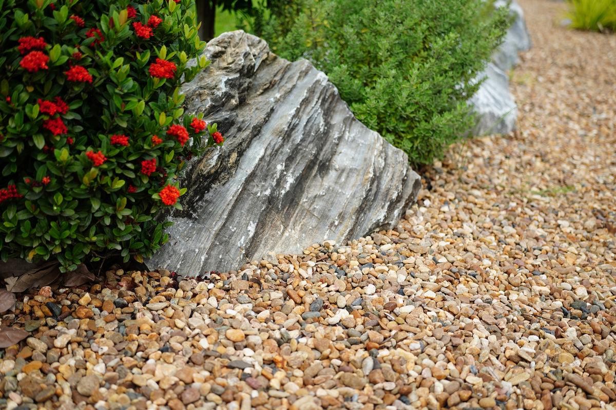 Decorative rock surrounded by pebbles and red flowers in a garden setting