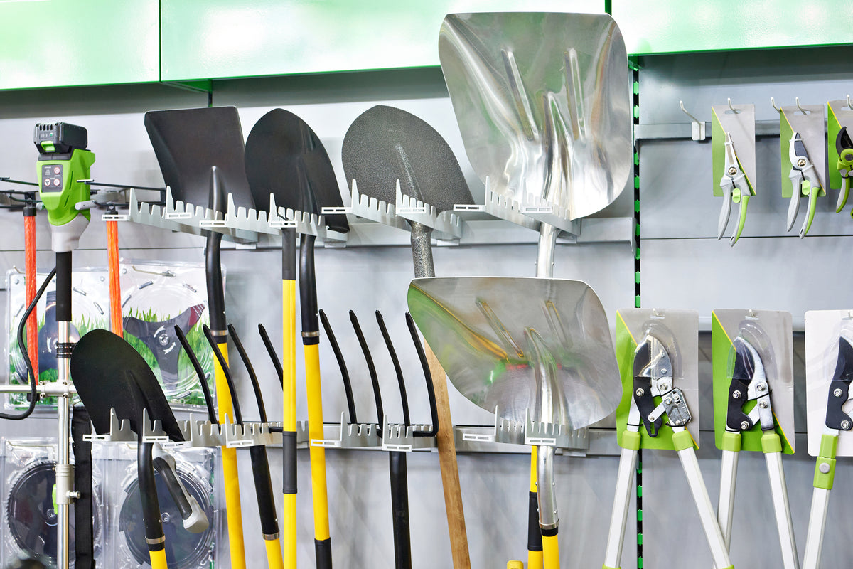 Set of shovels and rakes displayed on a wall rack with packaging in the background.